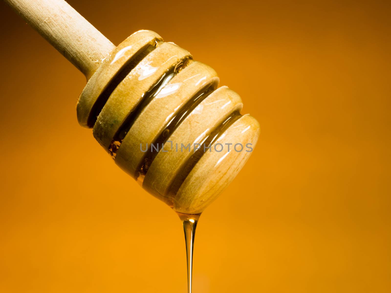 Honey drips off wood dipper into glass