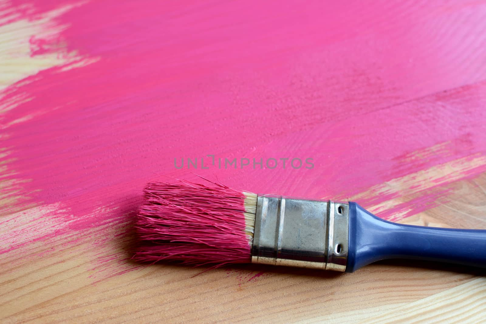 Paint-covered paintbrush on half-painted wooden board
