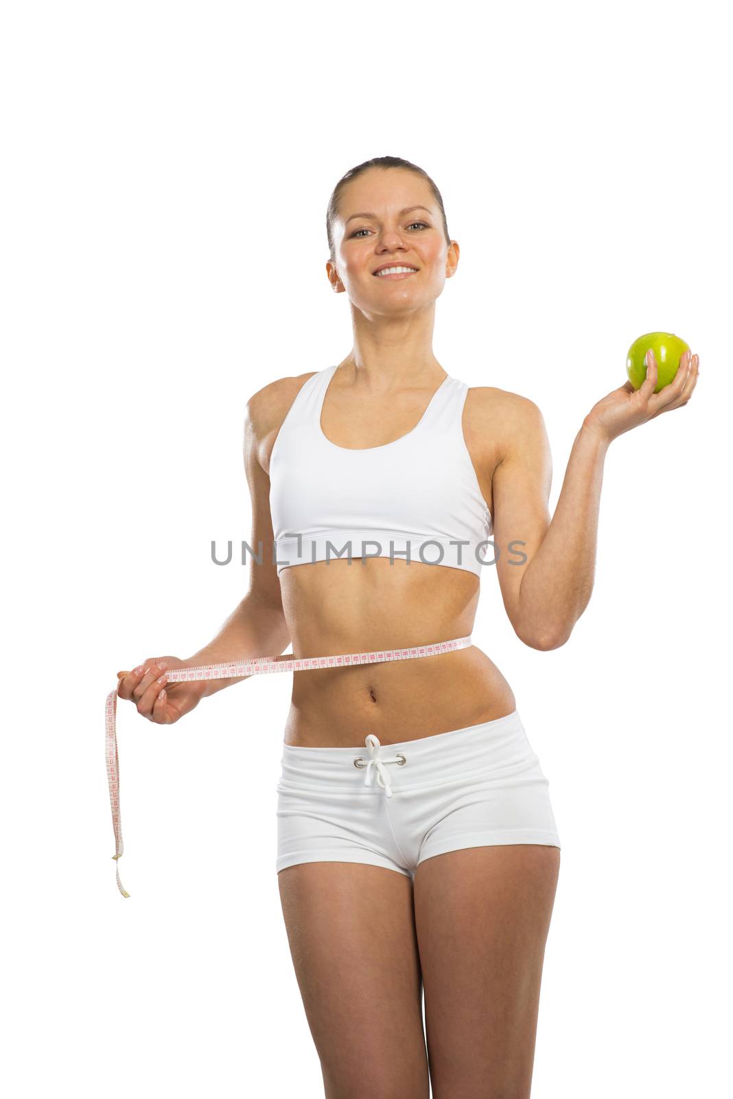young athletic girl measuring waist measuring tape and holding a green apple, concept of healthy eating, isolated on white background