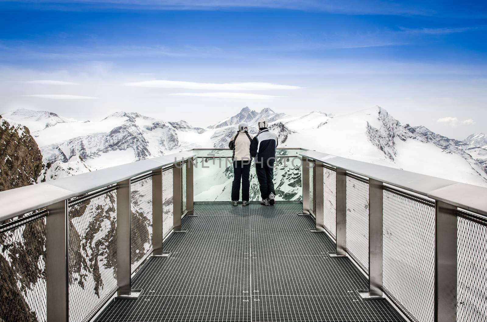 Two people looking at Alps mountains from viewpoint platform by martinm303