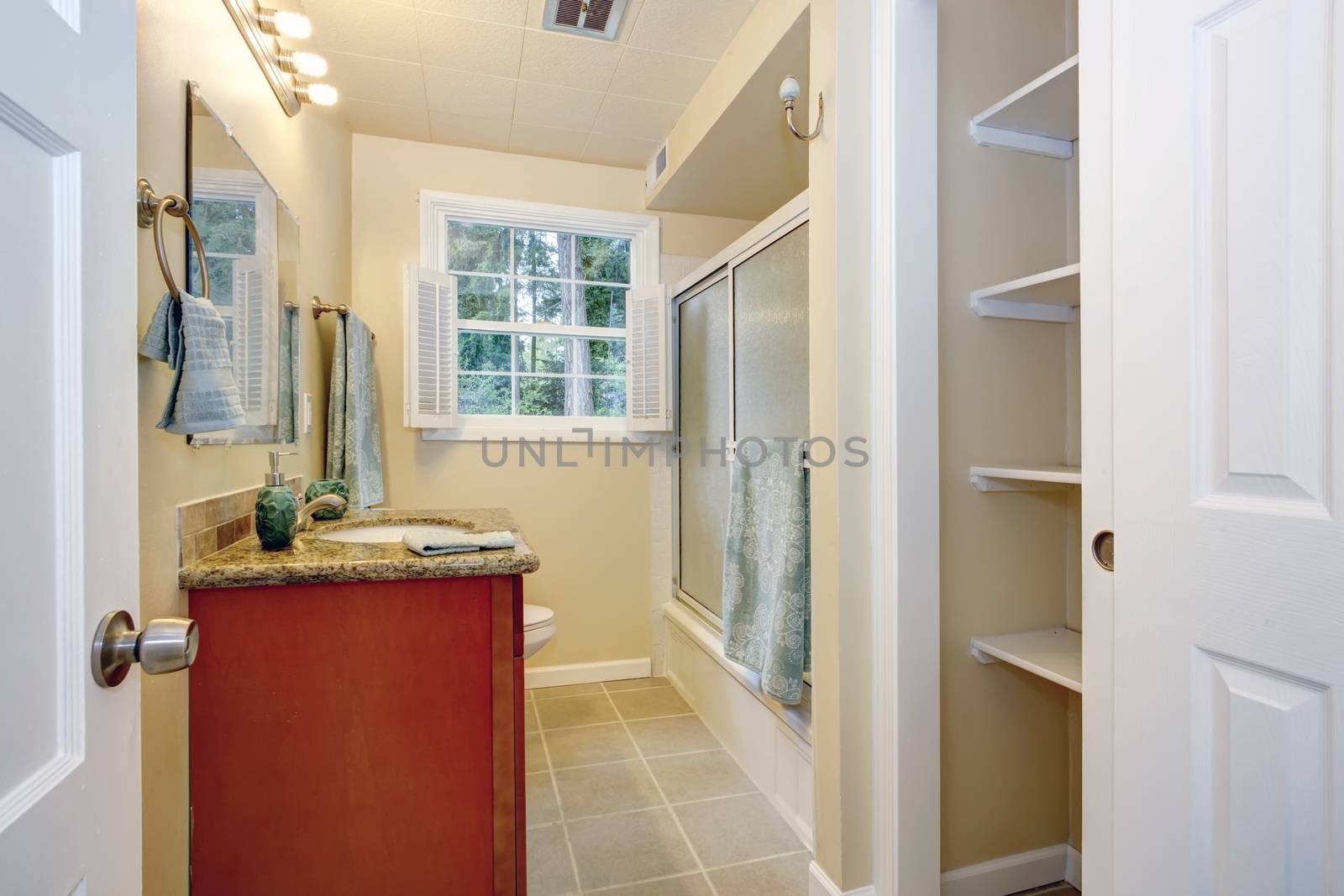 Light tones bathroom with french window. View of washbasin cabinet, bath tub with glass door and built-in shelves