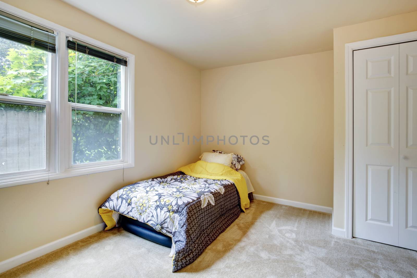Small bedroom with window, carpet floor. View of mattress covered with floral bedding