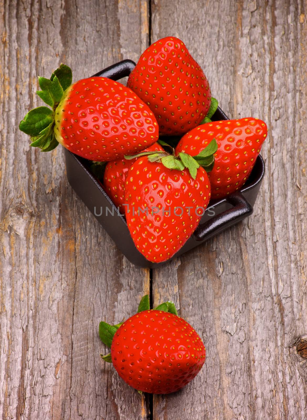 Stack of Perfect Raw Strawberries in Square Shape Black Bowl isolated on Rustic Wooden background