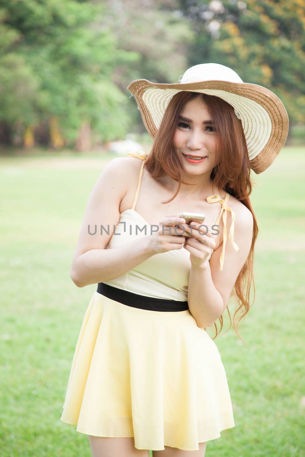 Asian woman smiling and holding a mobile phone. In the park
