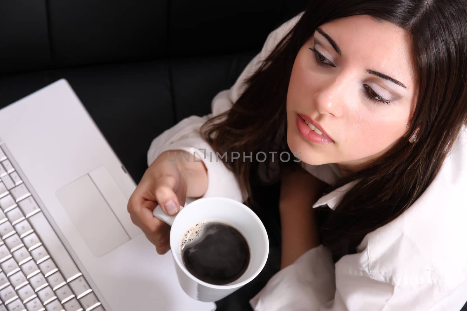 A young, hispanic adult girl watching a Laptop while drinking coffee.
