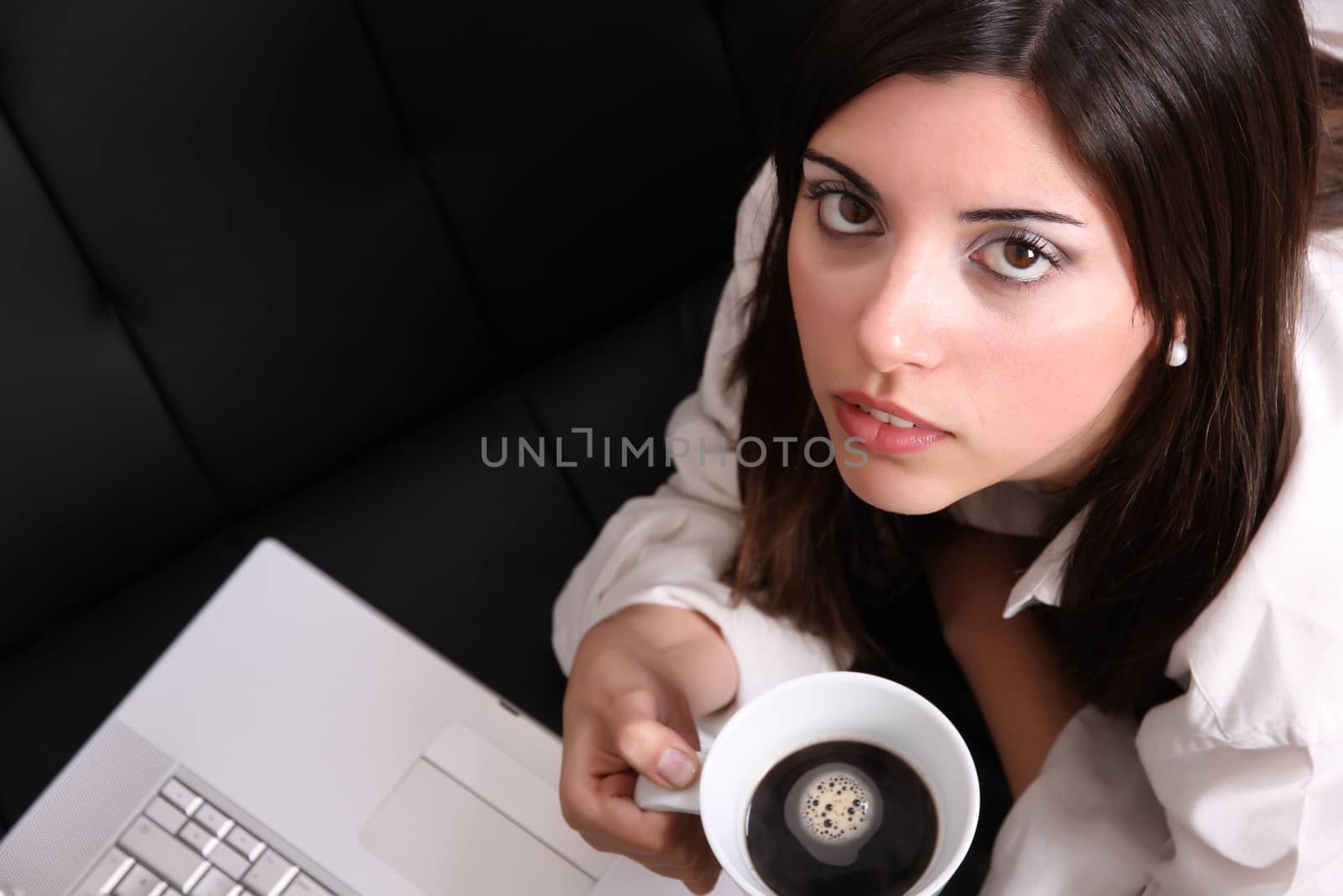 A young, hispanic adult girl watching a Laptop while drinking coffee.
