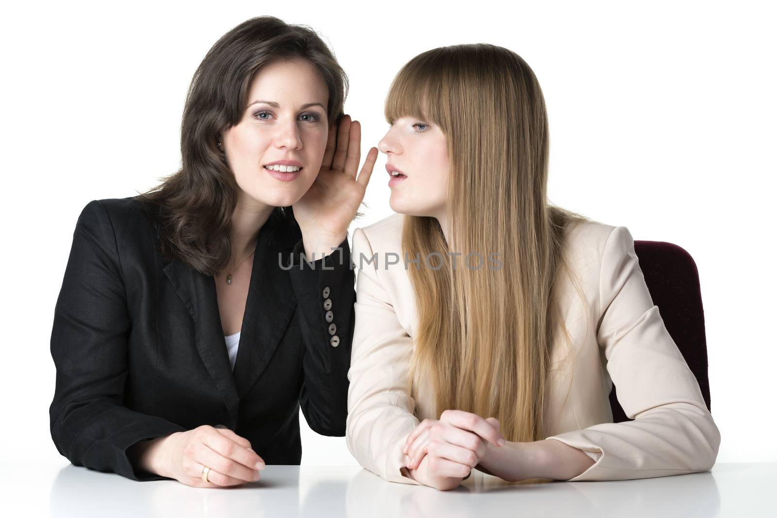 Two happy women blonde and brunette in a black and white jacket, sitting at a white table. Isolated on white background.