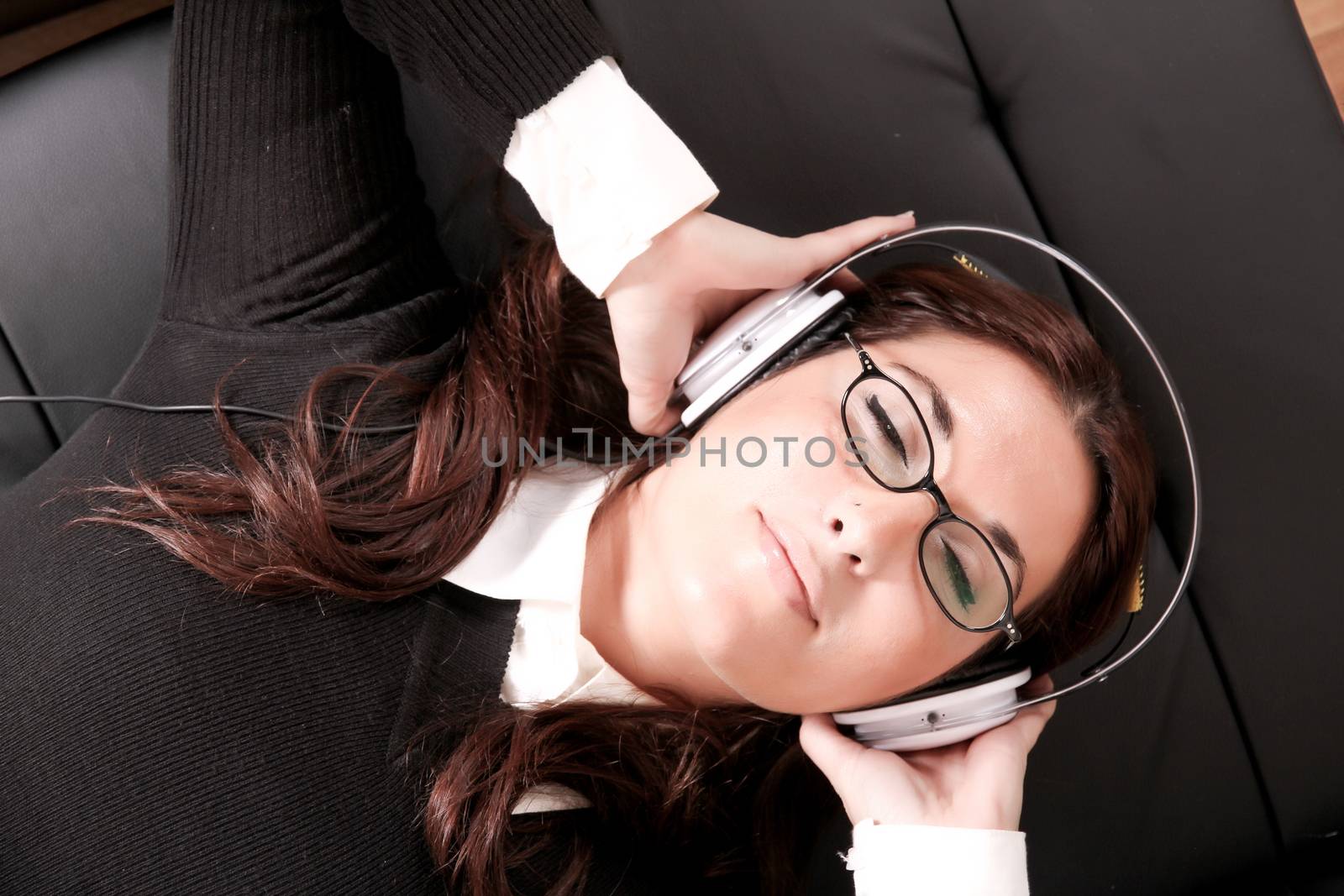 A girl listening to Music with headphones on the sofa.