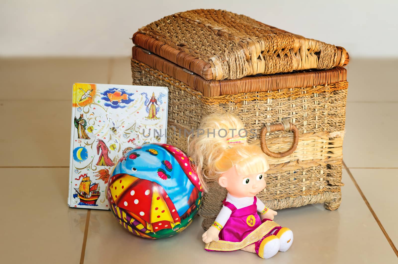 Beautiful children's toys: doll, ball, book. Are located near the container for storage of toys.