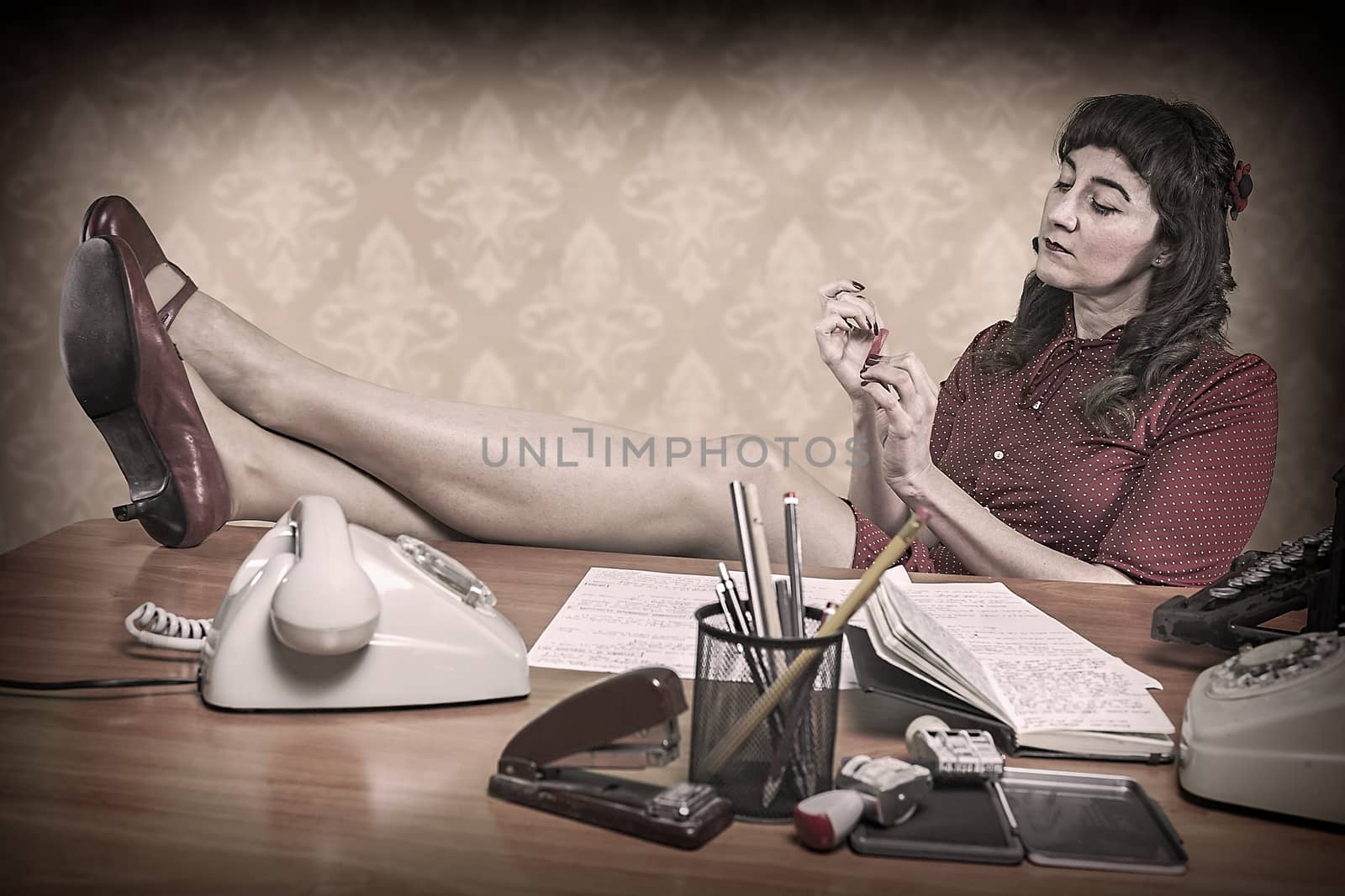 Young secretary with a nail file in the office, 1960's scene by digicomphoto