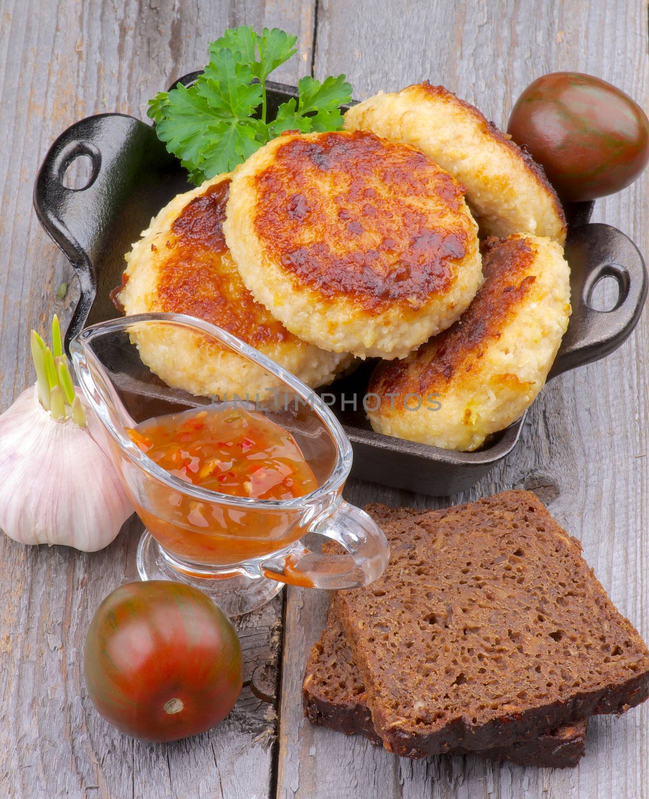 Arrangement of Delicious Chicken Meat Cutlets in Black Saucepan with Brown Bread, Sauce and Vegetables on Wooden background. Top View