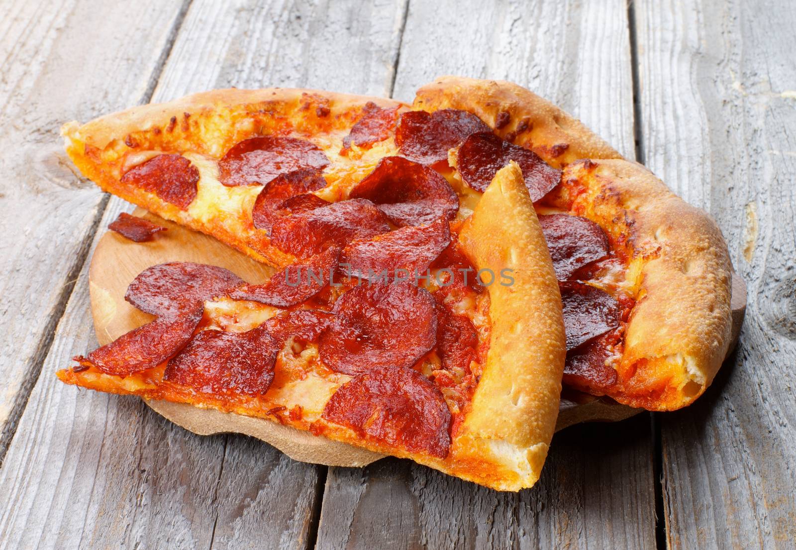Slices of Pepperoni Pizza with Tomatoes Sauce and Cheese on Wooden Plate closeup on Rustic Wooden background