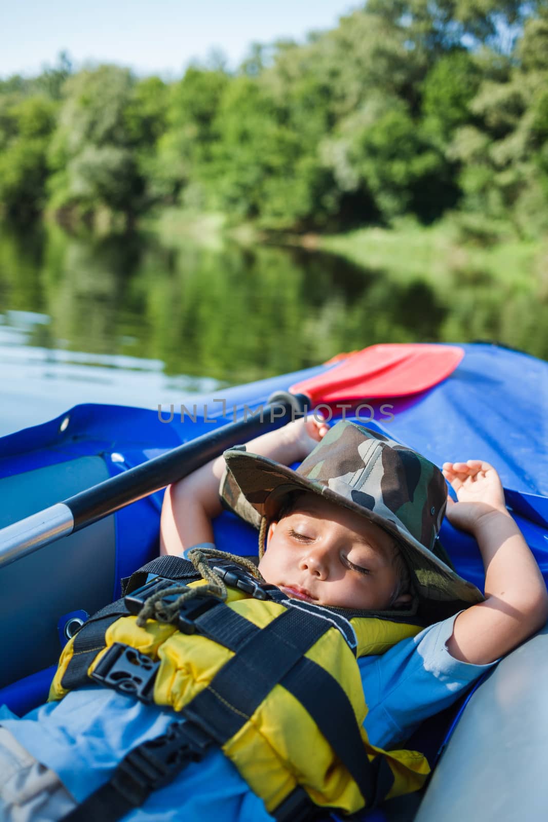 Cute little boy sleeping in kayak on the river at a lovely summer day.