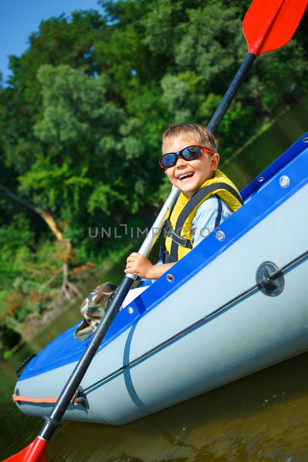 Happy little boy paddling kayak on the river and enjoying a lovely summer day