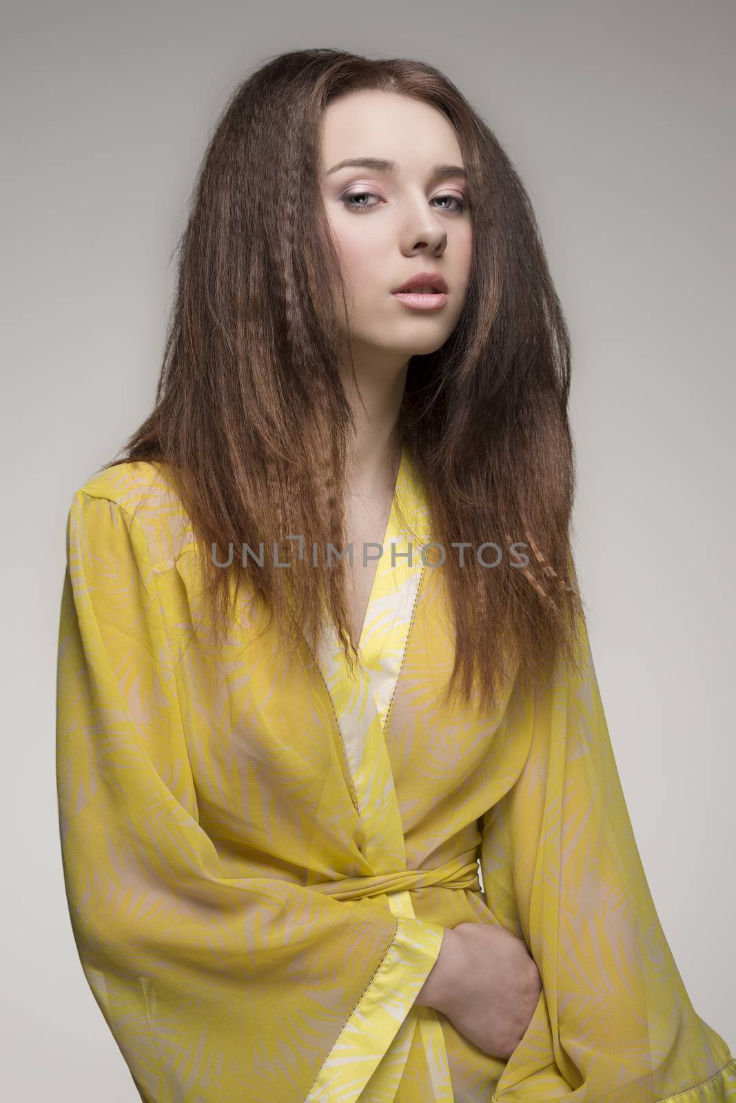 portrait of sensual brunette girl with long hair wearing yellow transparent nightgown and looking in camera