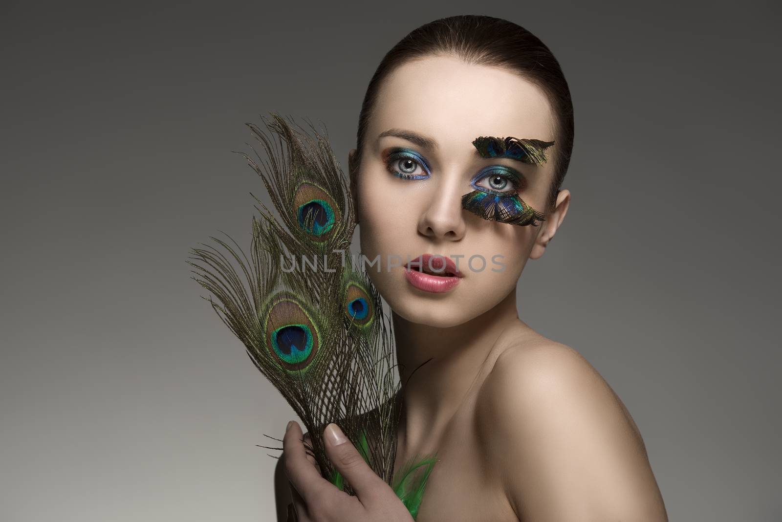 splendid naked brunette woman with make-up and accessory with colored peacock feathers. looking in camera