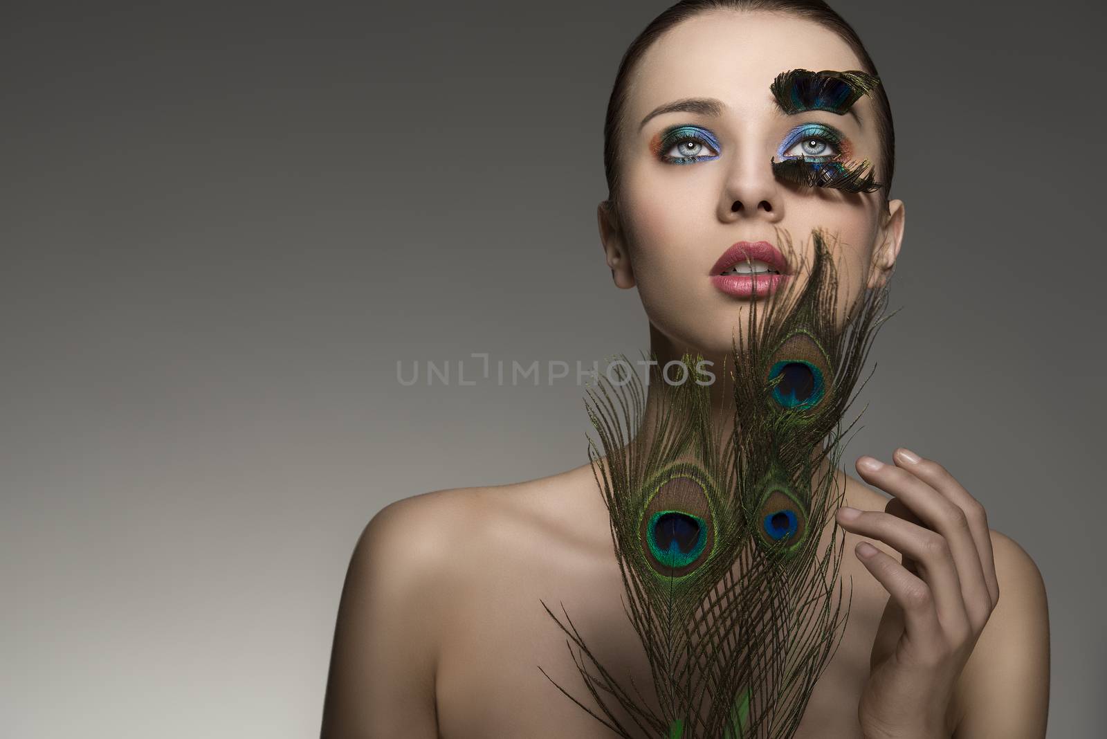 beauty close-up portrait of beautiful brunette lady with naked shoulders and peacock feather in make-up and accessory