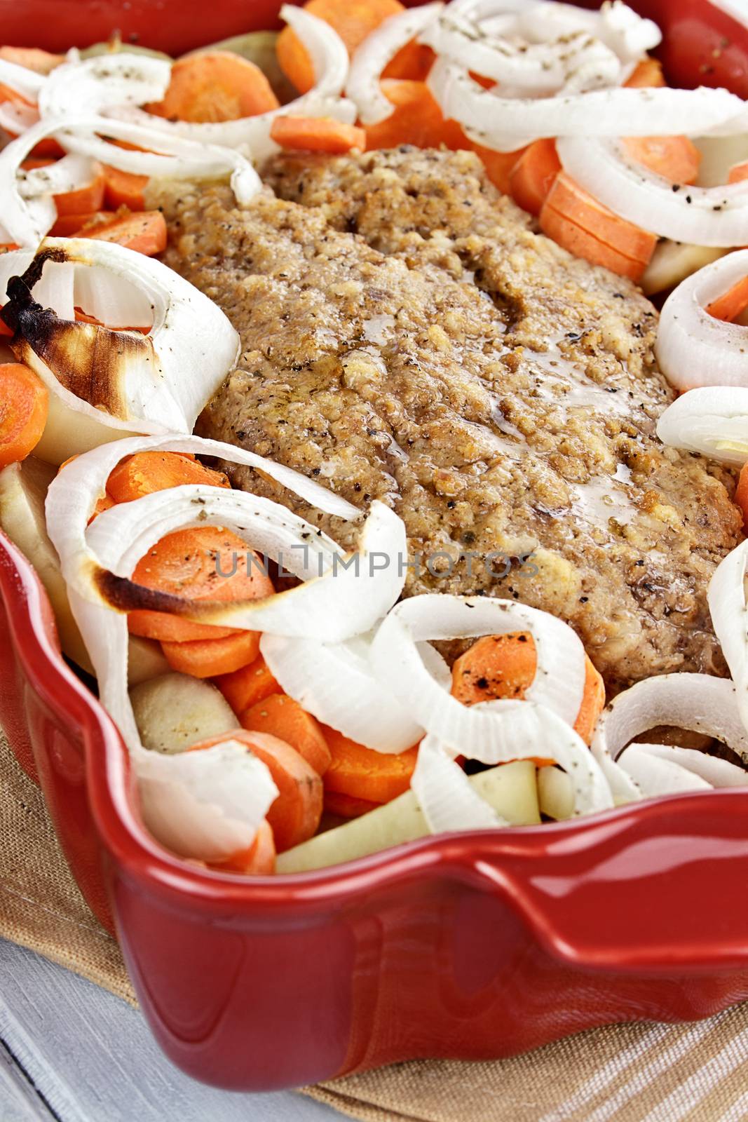 Casserole dish of freshly prepared meatloaf with onions, carrots and potatoes. Shallow depth of field.