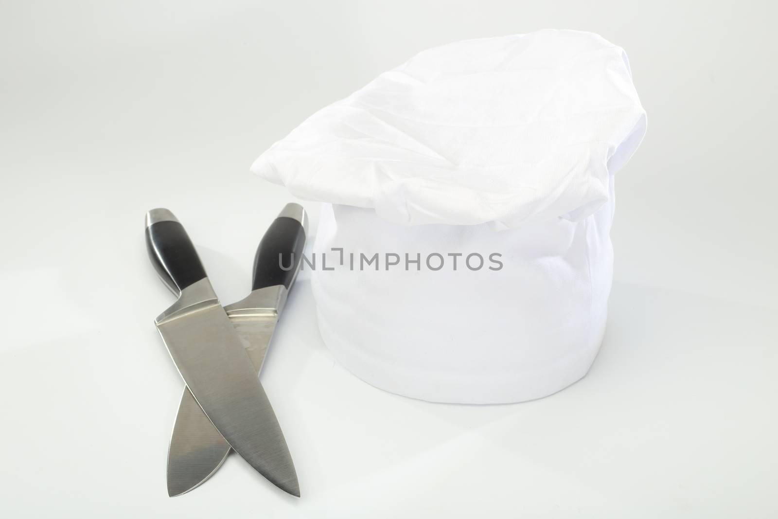  chef's hat and cooking knifes over white