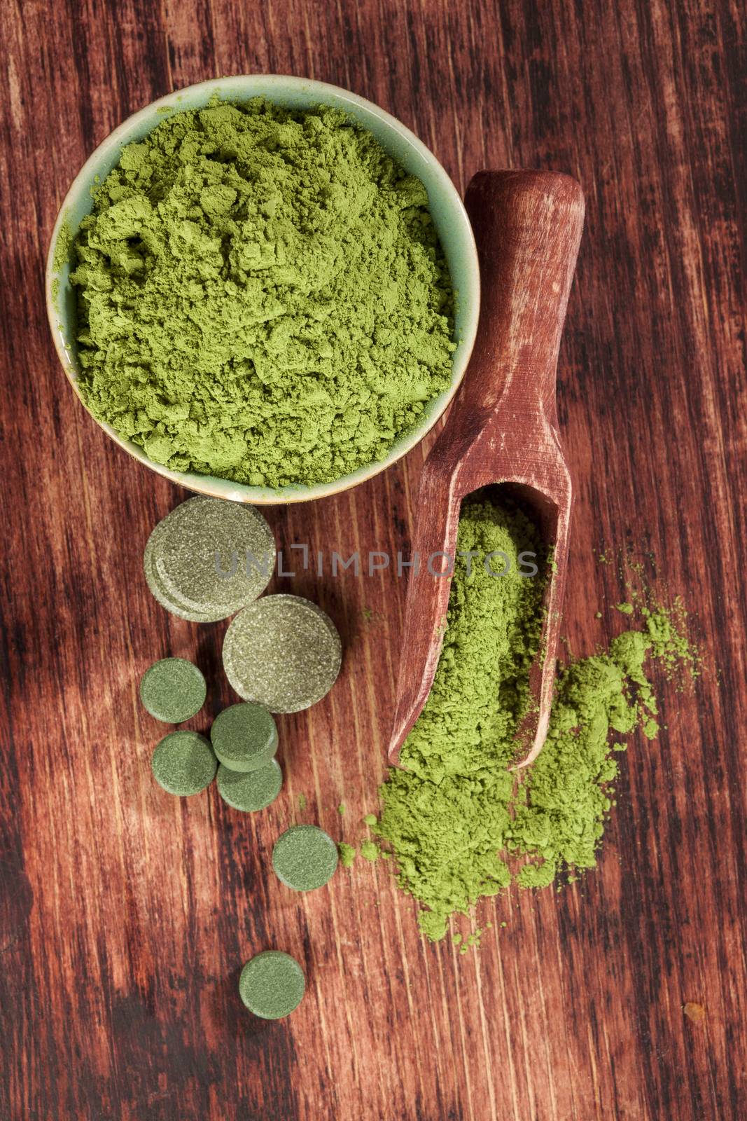Detox. Chlorella, spirulina and wheatgrass ground and pills with wooden spoon on brown wooden background, top view. Alternative medicine.