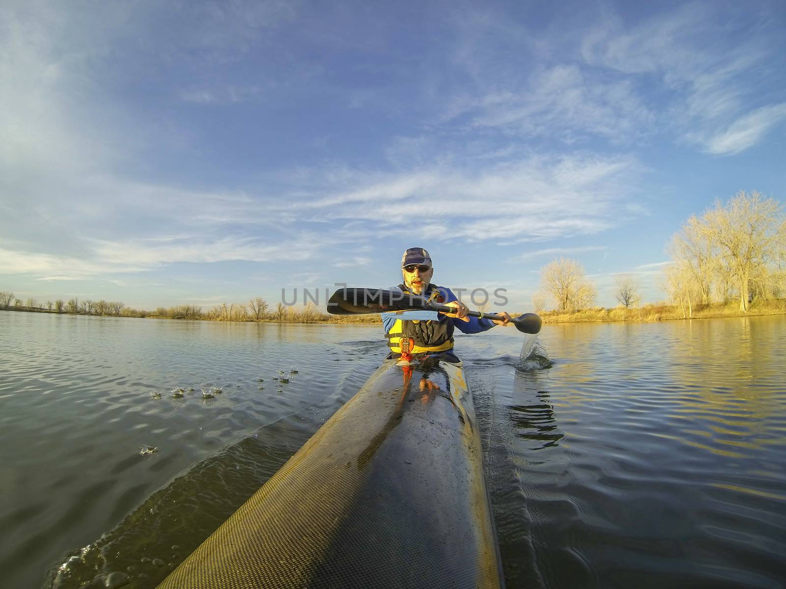 senior male paddler enjoys workout in a racing kayak in sunset light on a calm lake in Colorado
