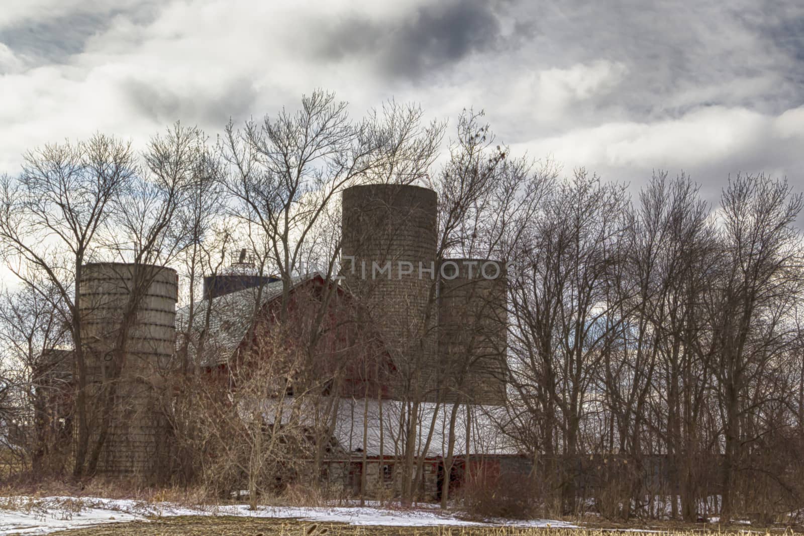 Large red barn surrounded by silos and trees. The sky is overcast with billowy clouds.