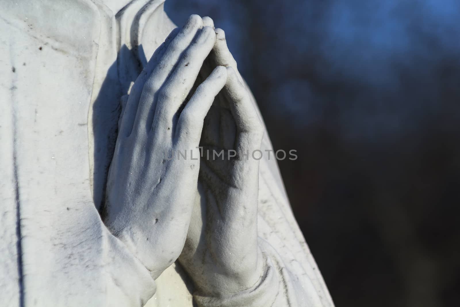 Stone statue of praying hands lit by the setting sun. 