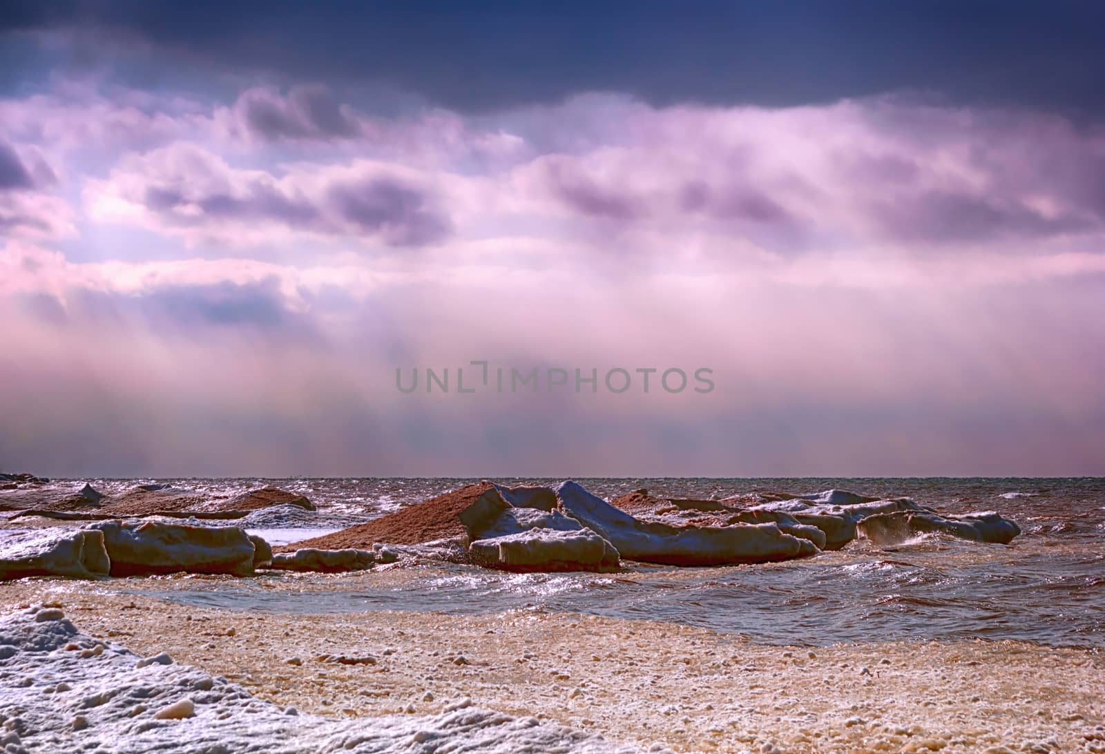 Shore line of Lake Ontario in the winter season. There is a purple glow to the sky. 