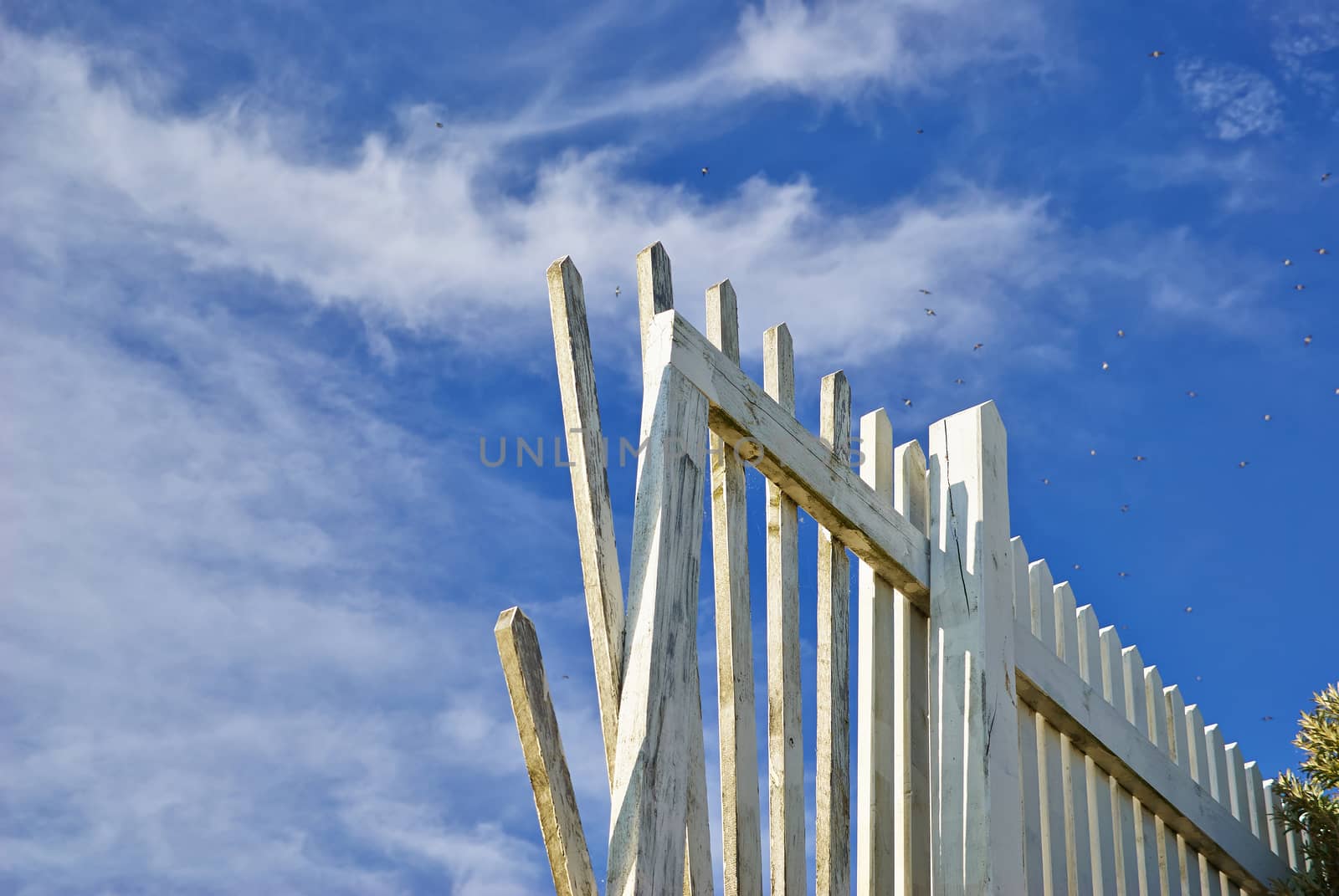Aging white wooden fence with cloudy blue sky background