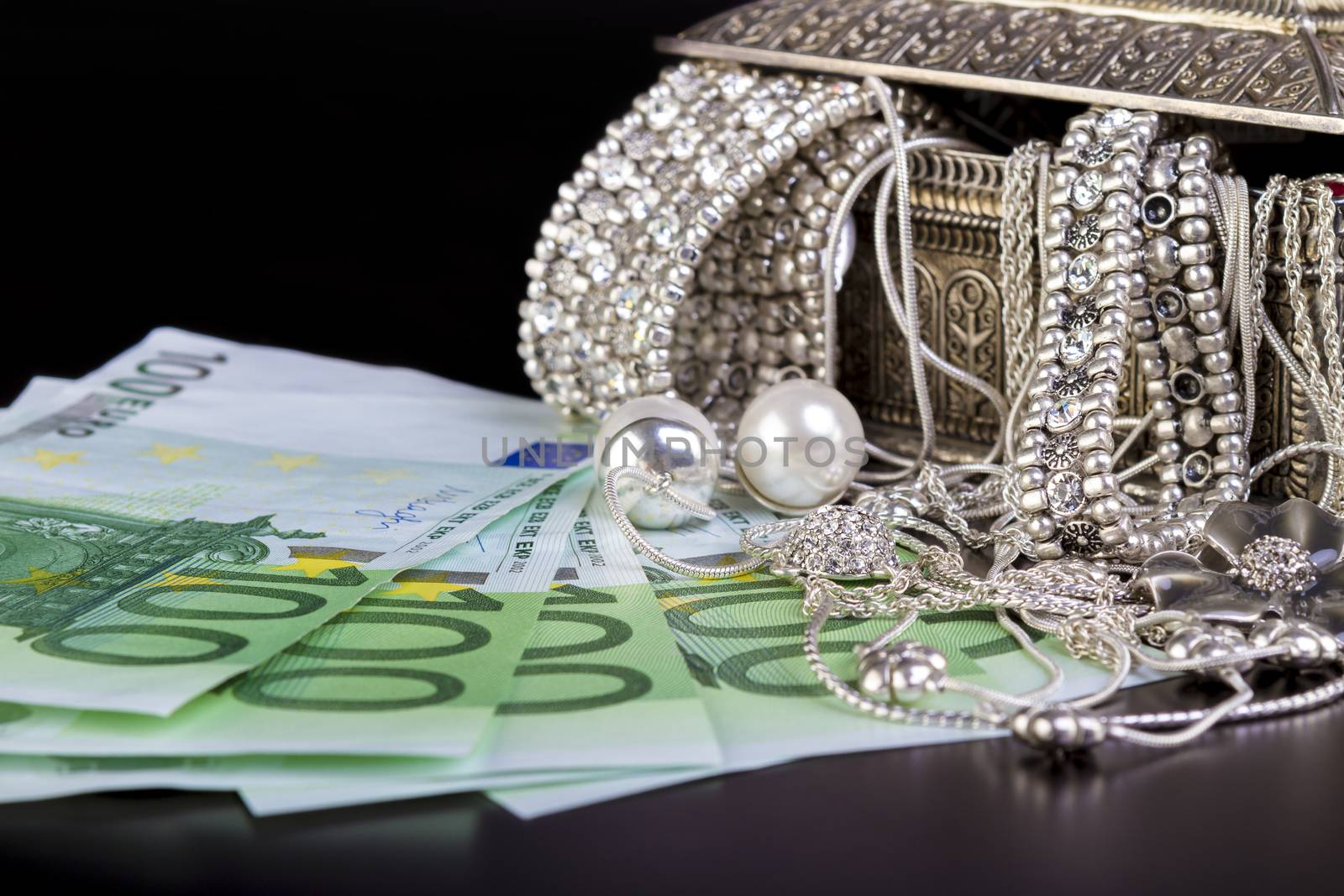 Silver jewelry and Euro on black by manaemedia