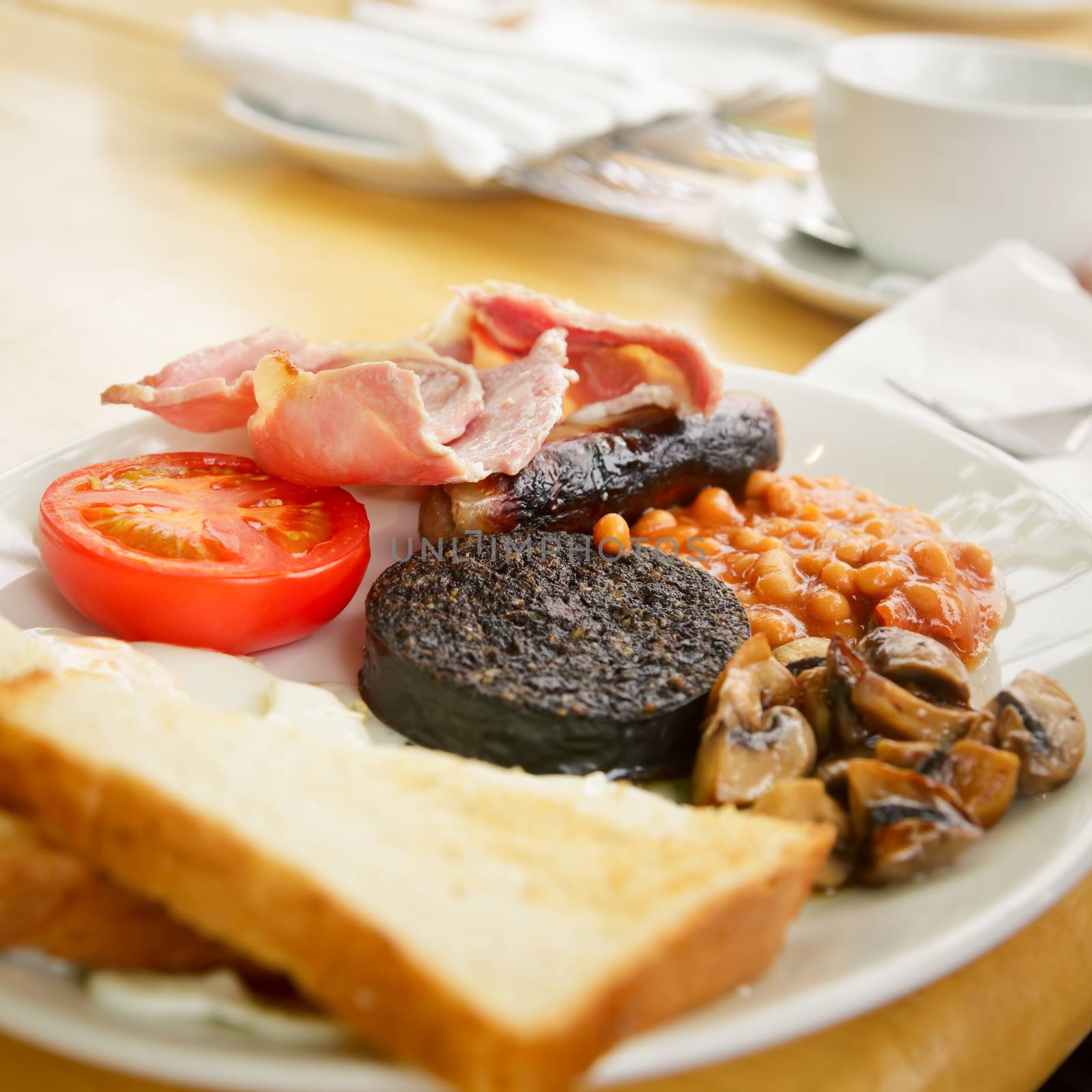 Plate with Full Scottish breakfast containing toasts, fried eggs, baked beans, grilled black pudding, sausage, tomato, mushrooms and bacon