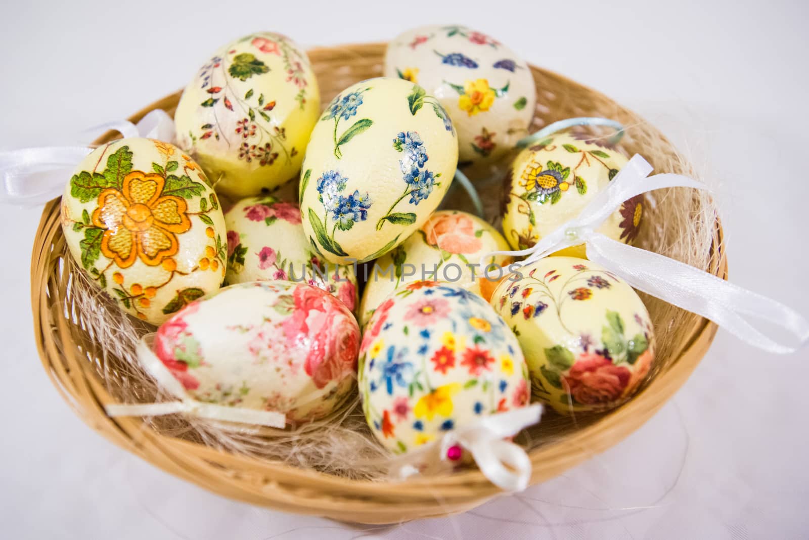 Group of colorful easter eggs decorated with flowers made by decoupage technique, in a basket on light background