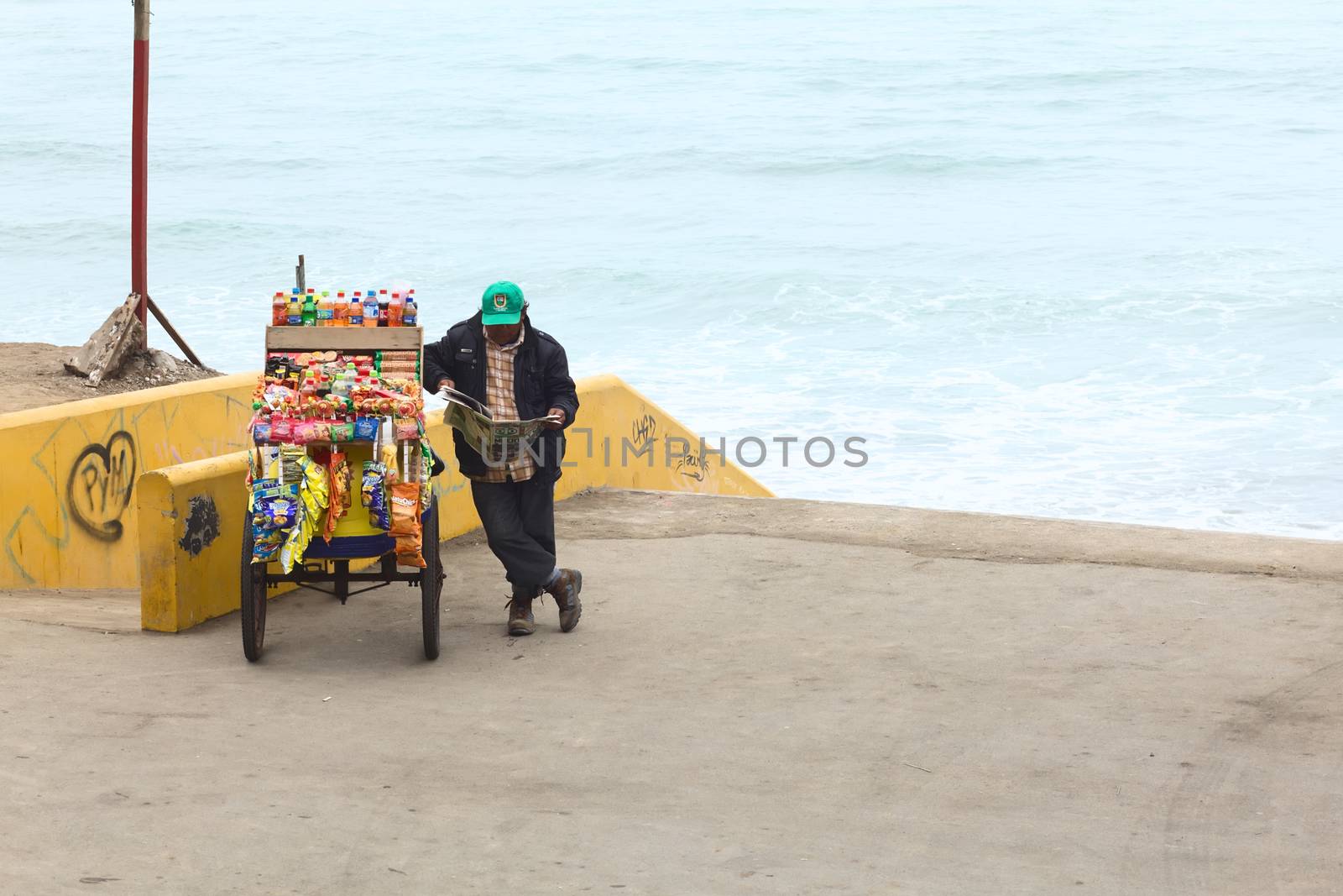 LIMA, PERU - JULY 5, 2013: Unidentified person reading a newspaper at snack cart filled with chips, sweets and drinks on the coast of Barranco on July 5, 2013 in Lima, Peru.  
