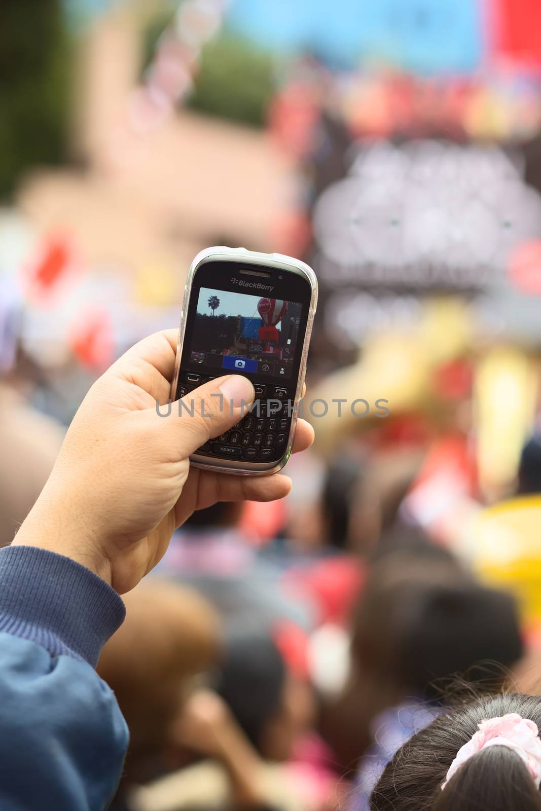LIMA, PERU - JULY 21, 2013: Unidentified person holding a Blackberry mobile phone to take a photo on the Wong Parade in Miraflores on July 21, 2013 in Lima, Peru. The Parade (Gran Corso de Wong) is a traditional parade to celebrate the Peruvian national holiday which is on July 28-29. 