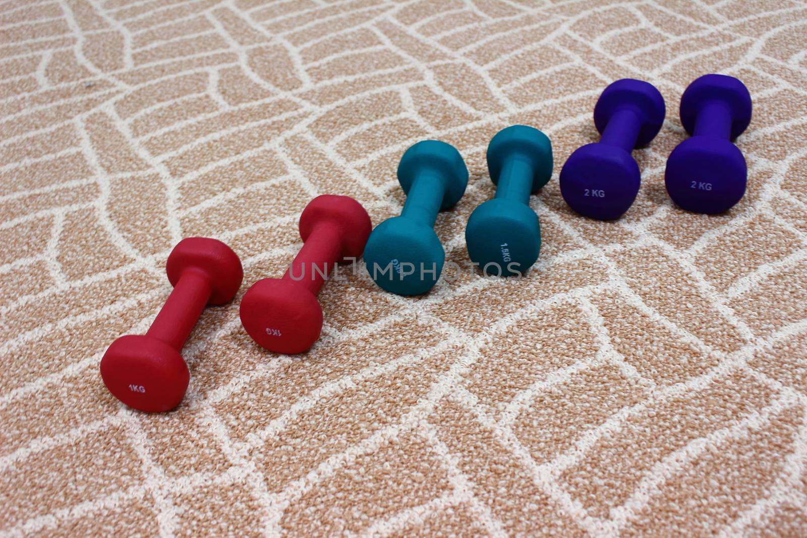 On the brown carpet on three pairs of dumbbells of different weights and different colors for sports