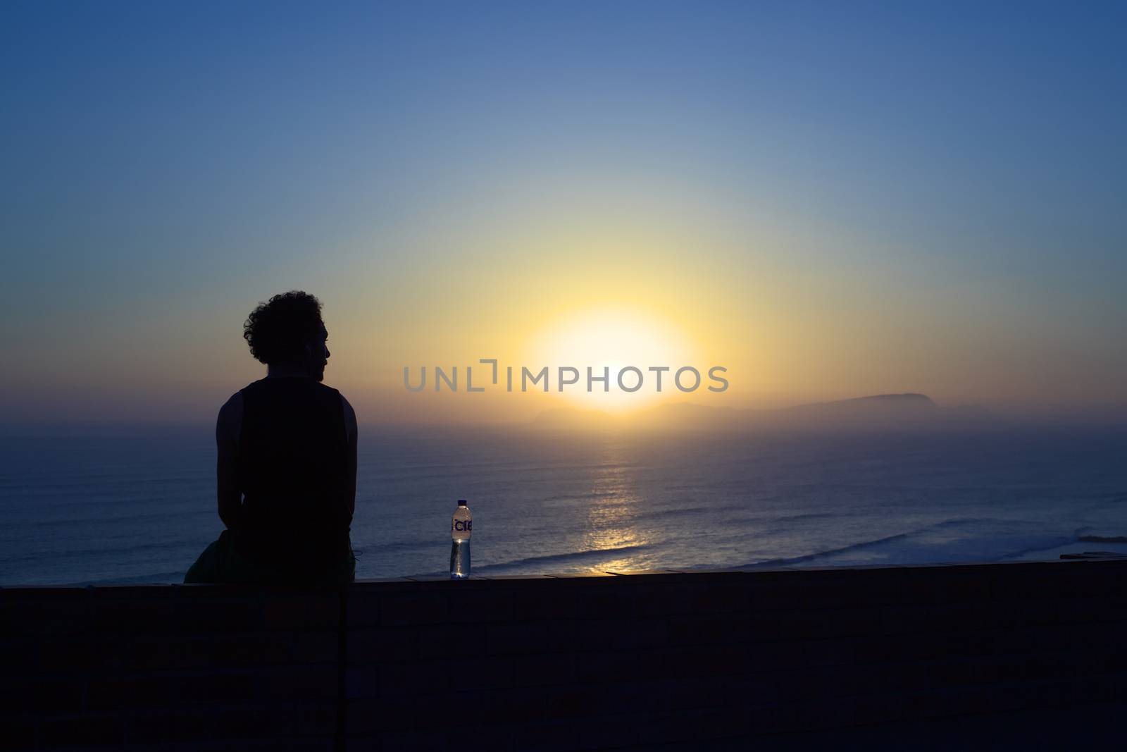 LIMA, PERU - MARCH 30, 2012: Unidentified young man watching the sun setting over the island San Lorenzo in the Pacific Ocean on March 30, 2012 in Miraflores, Lima, Peru.
