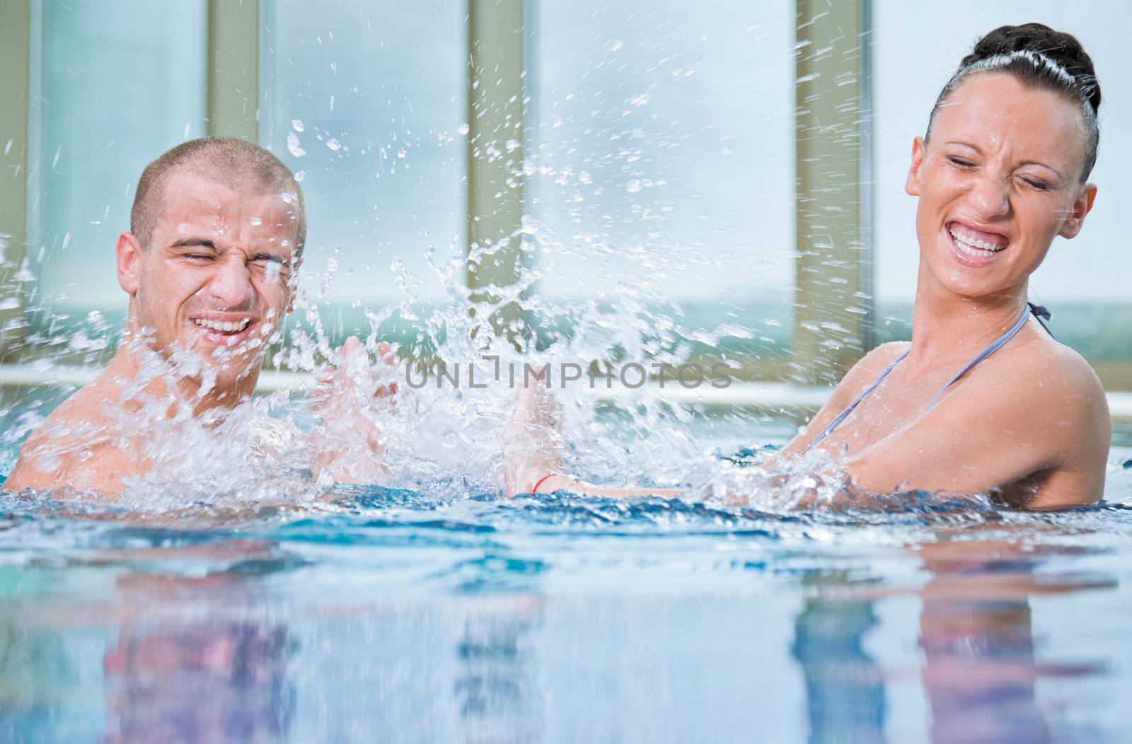 Young attractive female and handsome male splashing in a swimming pool