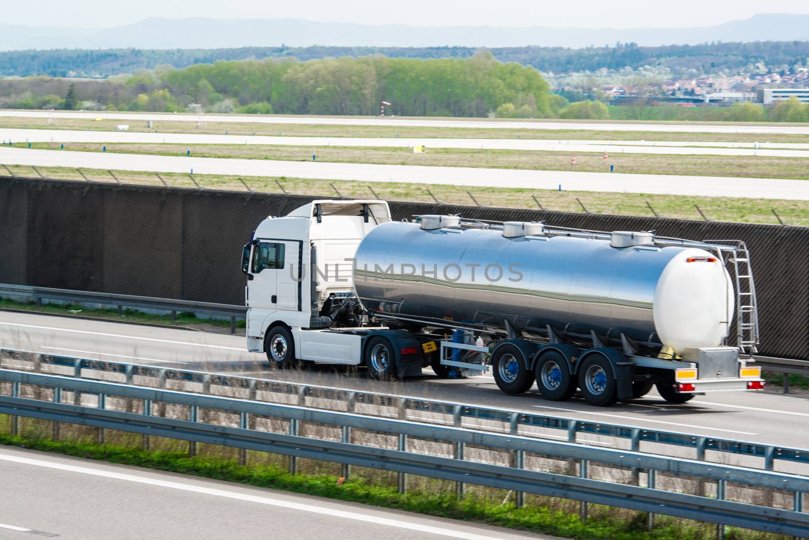 big fuel gas tanker truck on the highway next to the runway of an airport with space for your company logo and text