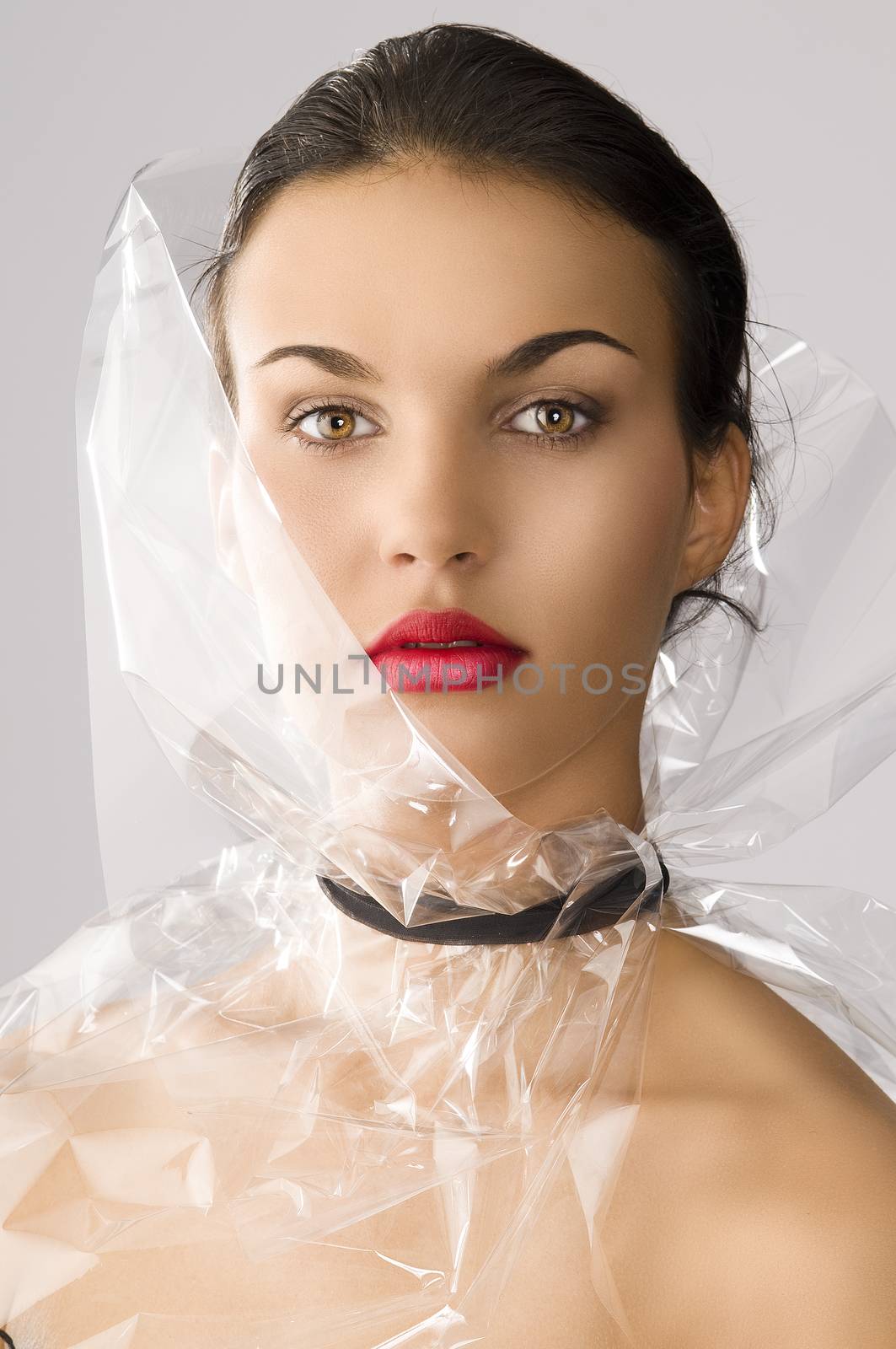 beauty portrait of young brunette with red lips and cellophane around her face, she is in front of the camera and looks in to the lens