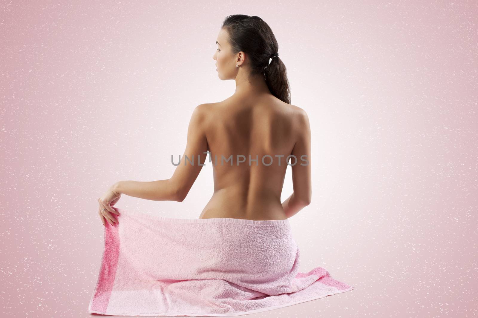 naked brunette showing her back shoulder and covering her body with a pink towel