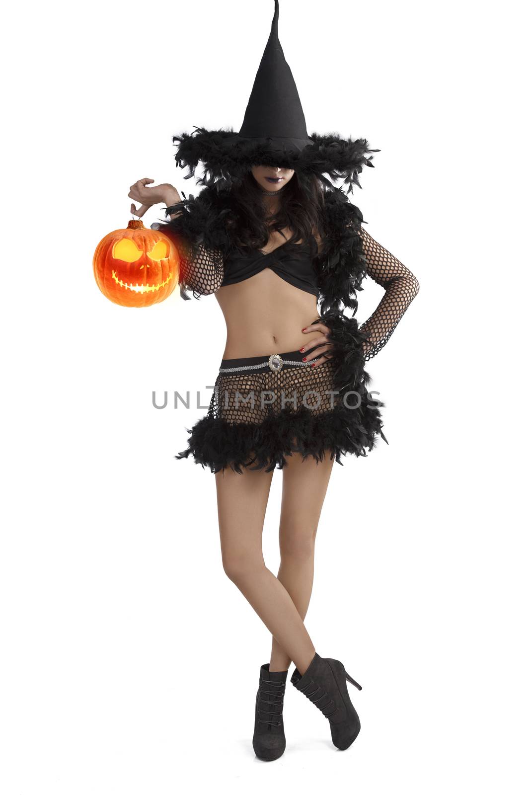 very pretty young brunette in black witch dress with hat and high heel ready for halloween standing with party ball against white background