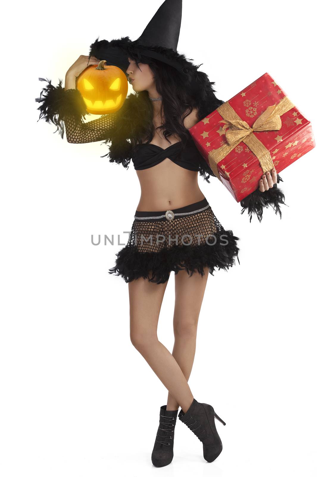 very pretty young brunette in black witch dress with hat and high heel ready for halloween standing with gift box and jack-o'-lantern