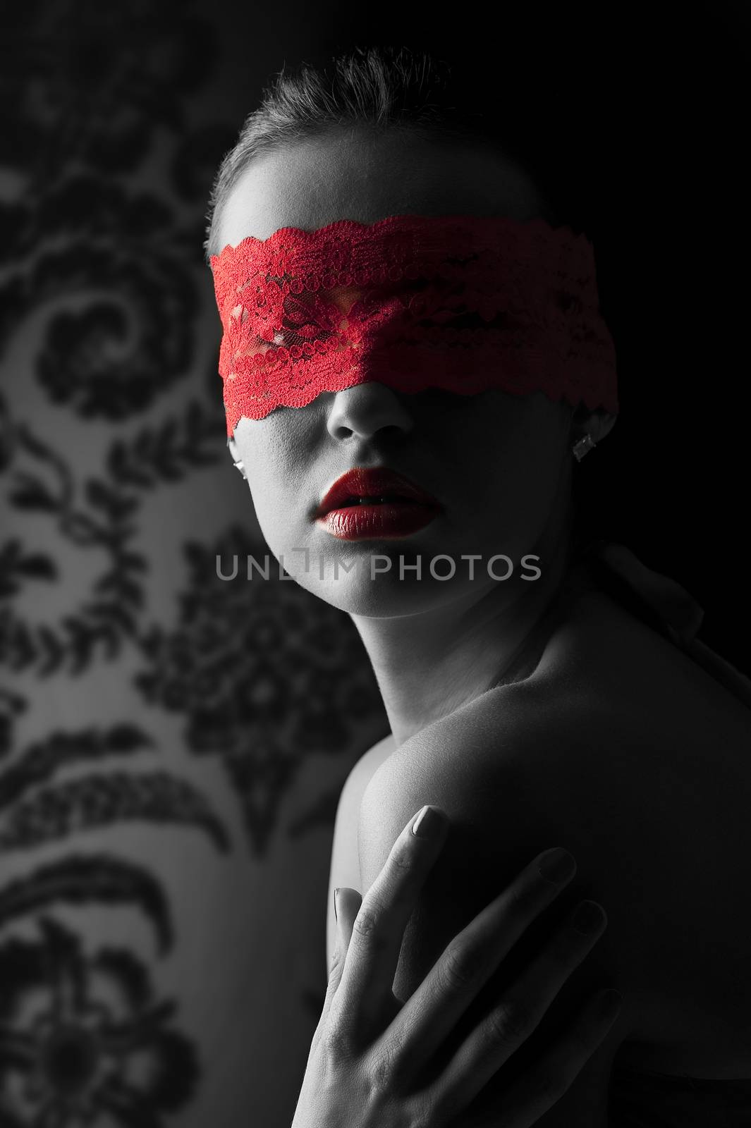 sensual portrait of a young brunette on black background with a red mask of lace