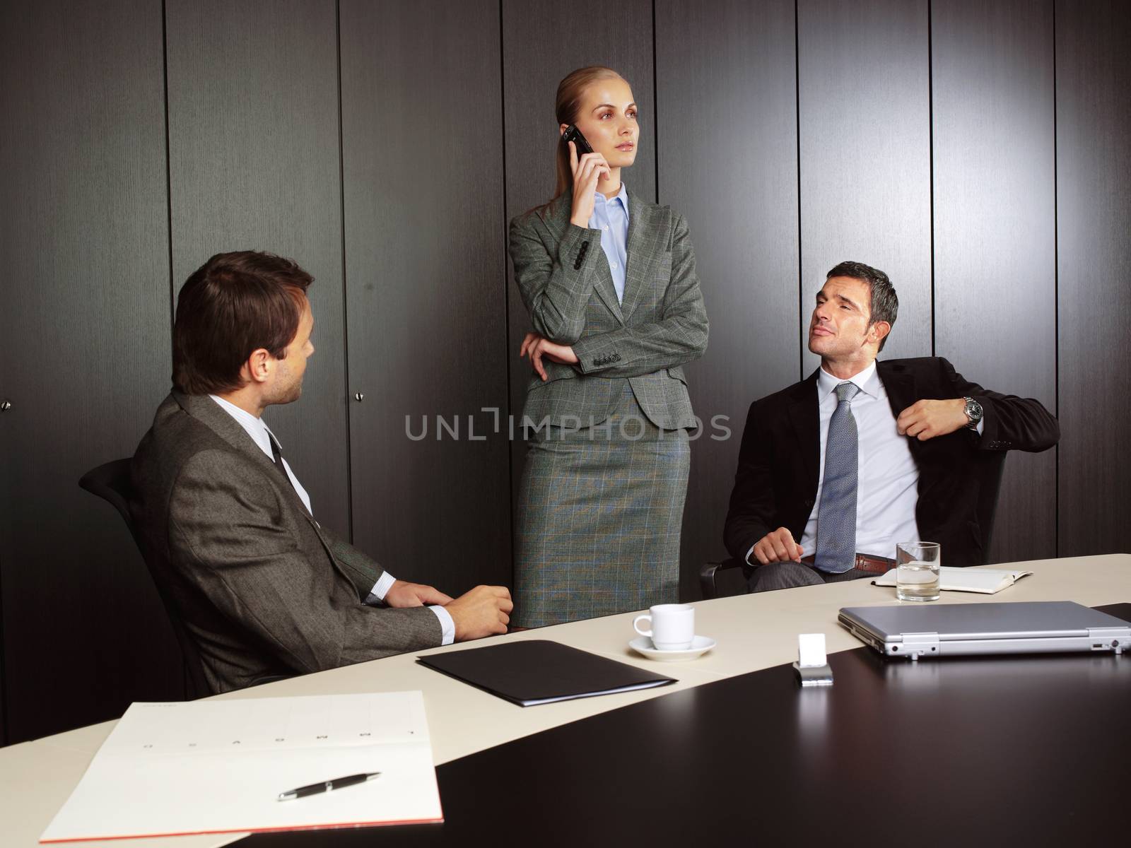 Young businessman explaining to businesswoman at office sitting on table talking on mobile