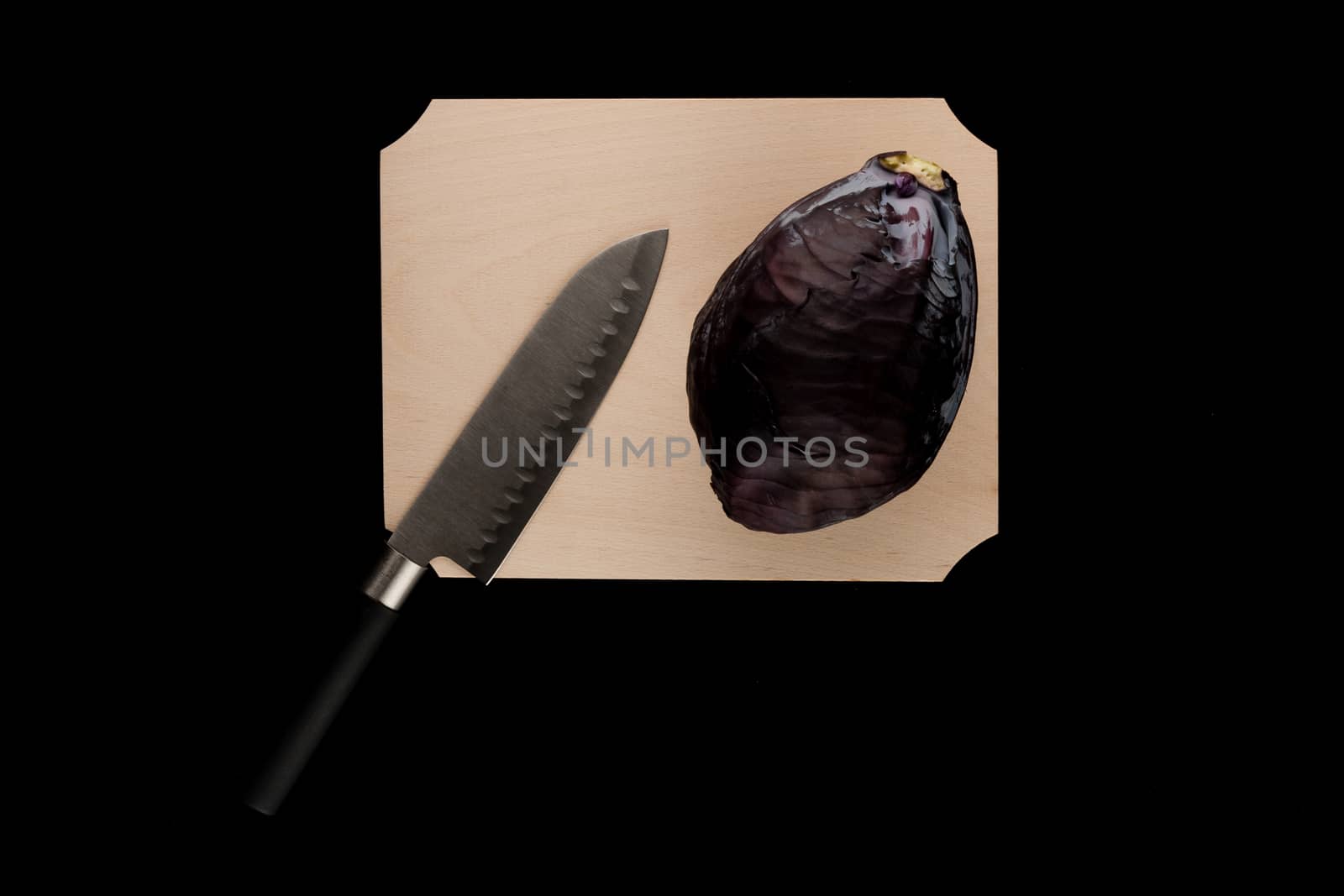 red cabbage with knife on wooden cutting board on black background
