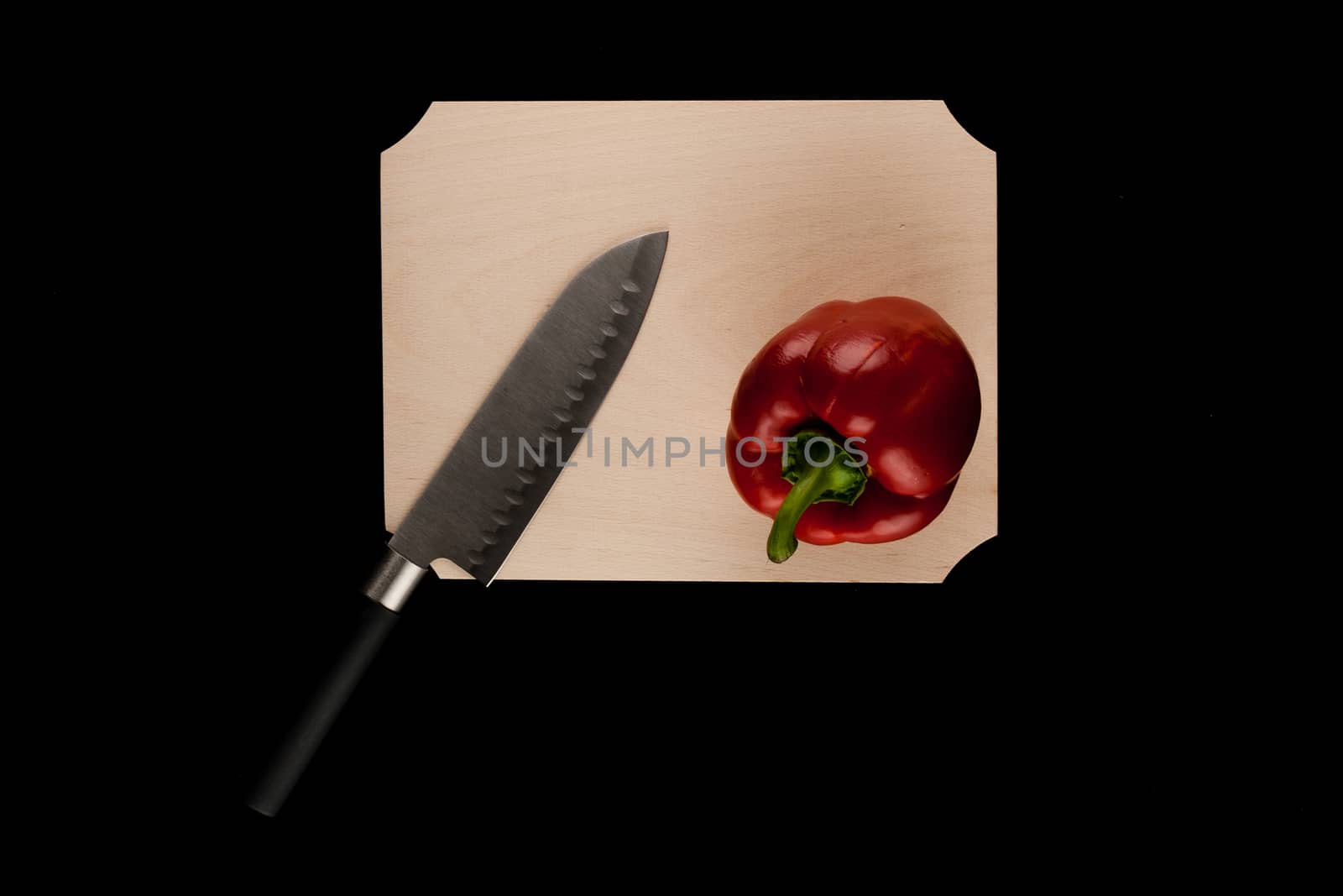 pepper with knife on wooden cutting board on black background