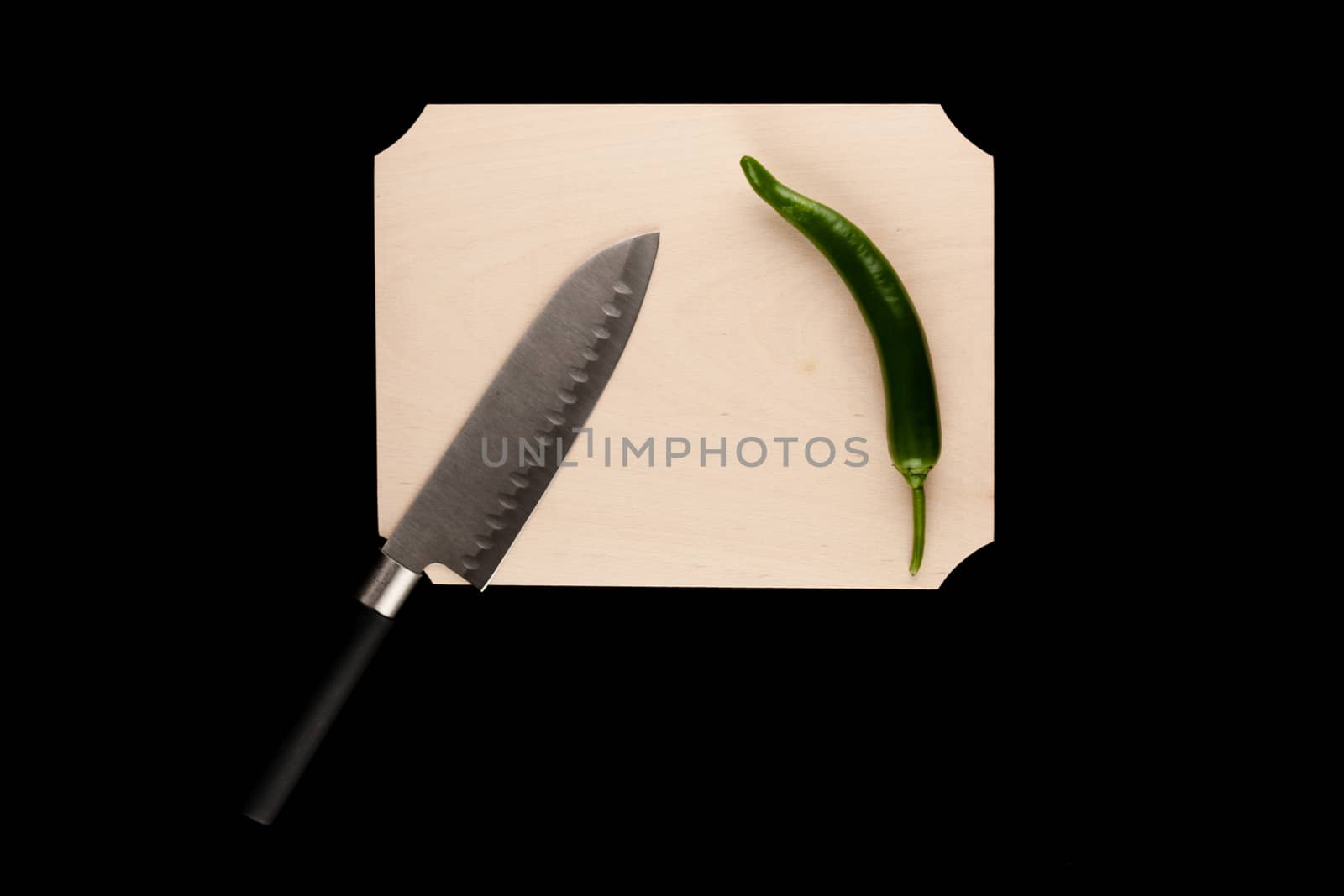 pepper with knife on wooden cutting board on black background