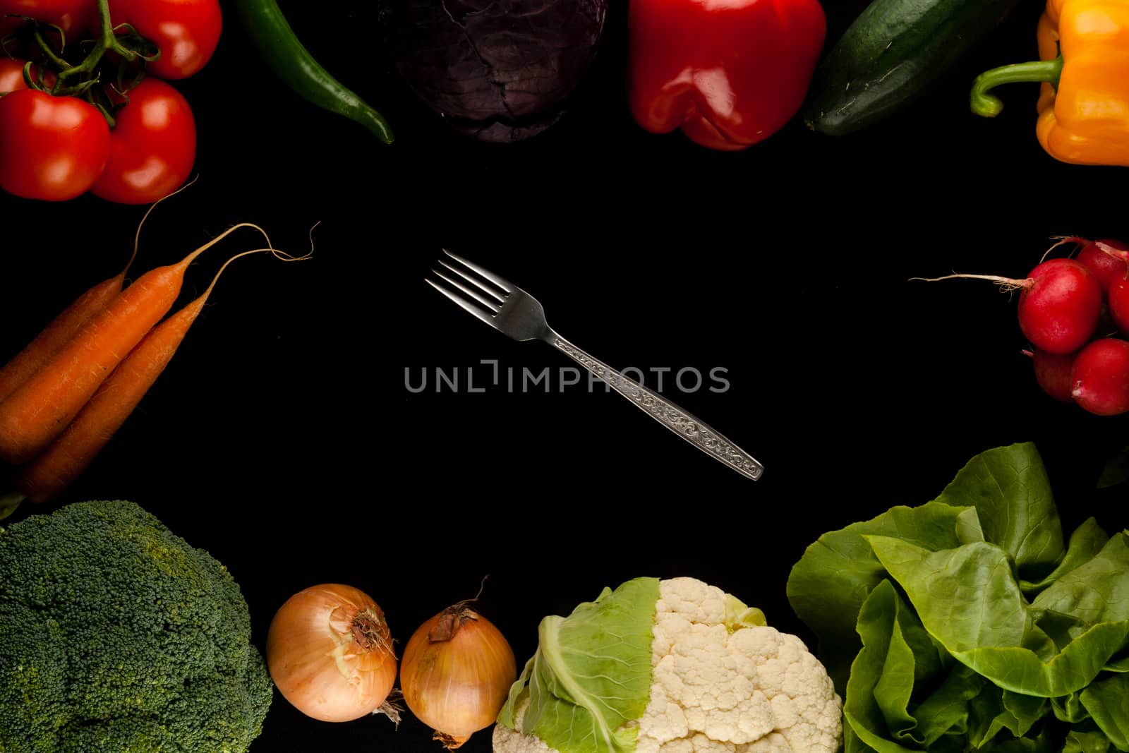 border made of different vegetables with fork in the middle on black background