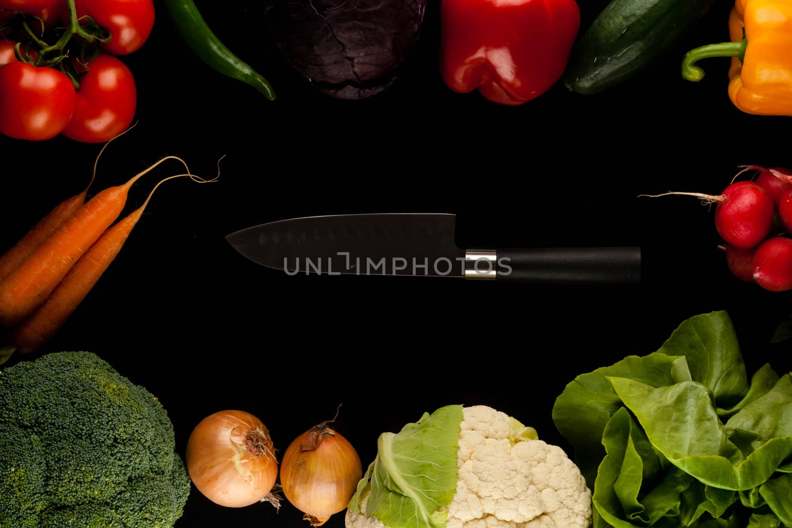 border made of different vegetables with knife in the middle on black background