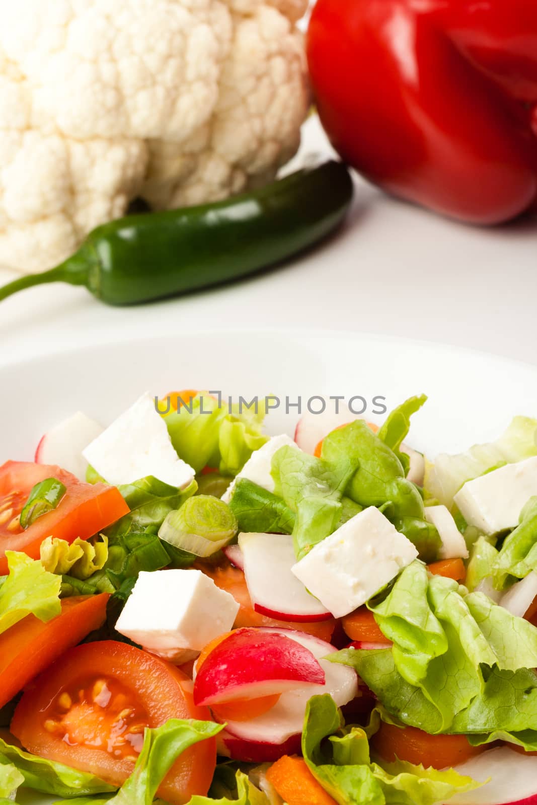 vegetable salad in white bowl with different vegetables in the background